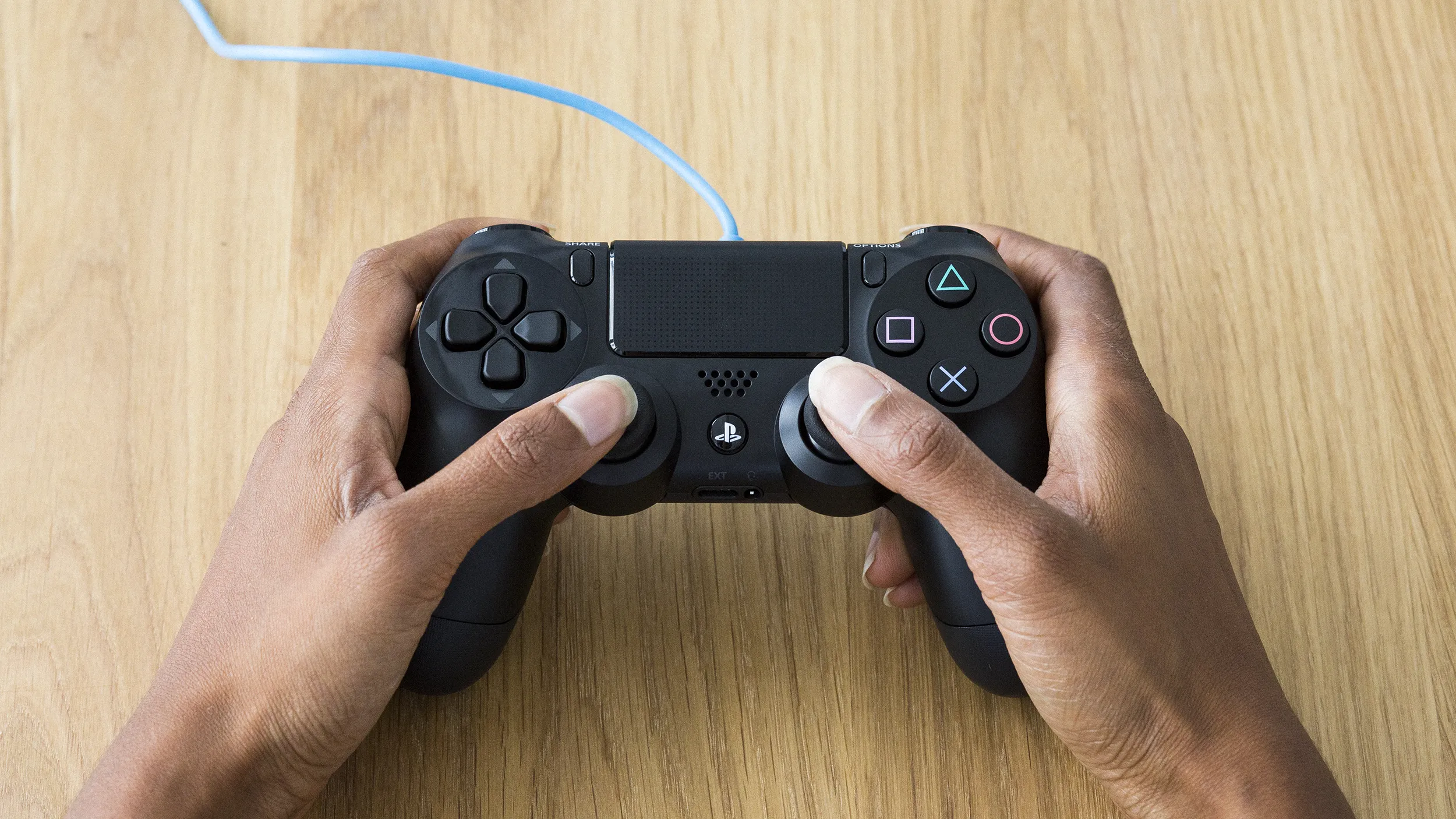 Close up of two hands holding a wired PlayStation controller.