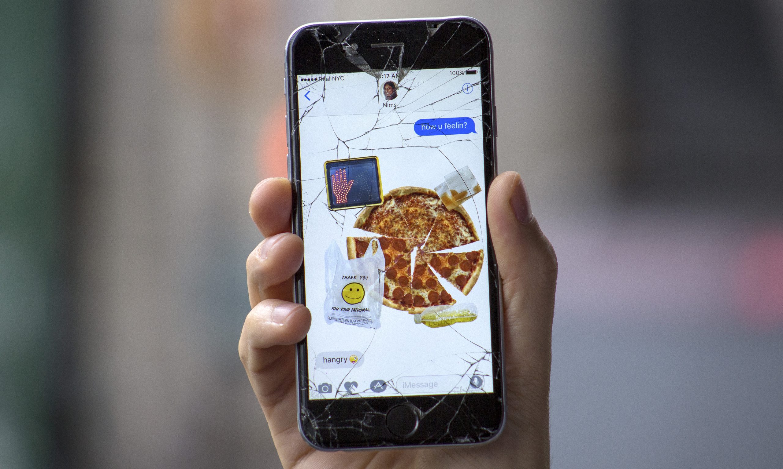 A cracked iPhone showing a collage of stickers making a pizza with garbage on it.
